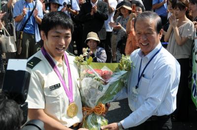 庁舎前で大勢の市民や職員の歓迎を受け、須田健治市長から米満達弘選手に花束が贈呈された時の写真です。