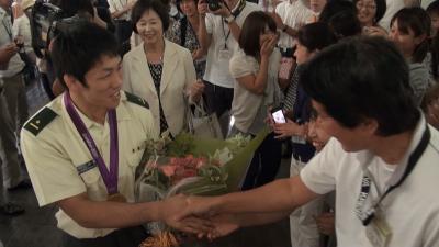 庁舎内で、大勢の市民に囲まれ、握手の求めに応じている米満達弘選手の写真です。
