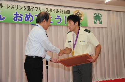 市民栄誉賞を受け取った米満達弘選手が、須田健治市長と握手している場面の写真です。