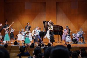 堀家さんと子どもたちがステージで演奏している写真です。